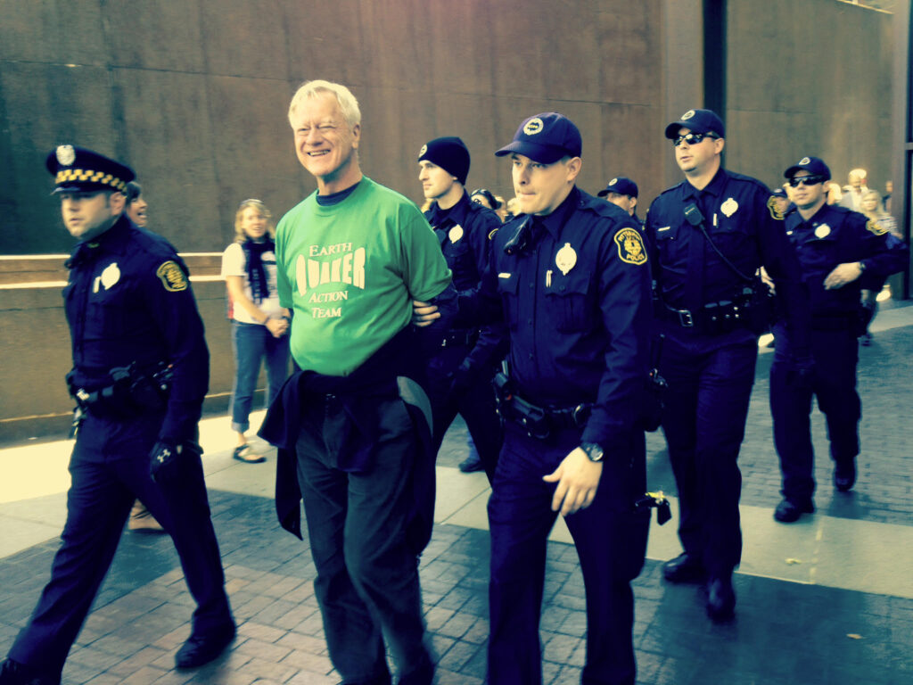 George Lakey smiling while being arrested and flanked by numerous police officers.
