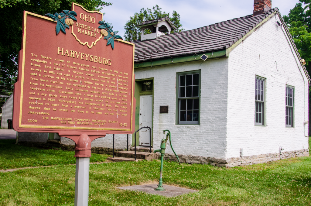 A historic white one-story building with a historical marker out front.